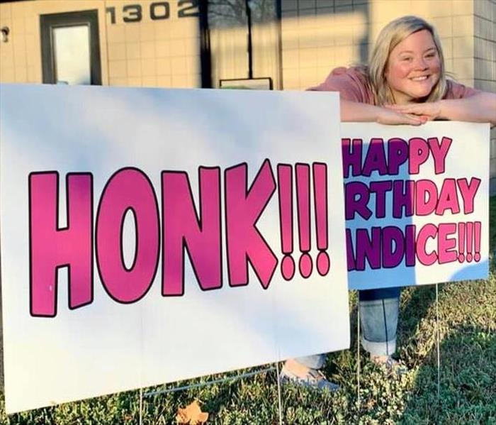 A woman standing behind signs that say it is her birthday