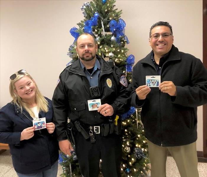 Two people posing with a cop while holding gift cards.